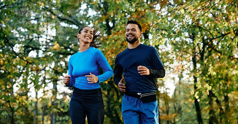 Young happy athletic couple jogging while exercising in park.