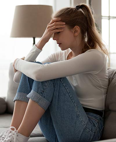 Upset woman frustrated by problem sitting on couch, embracing knees,