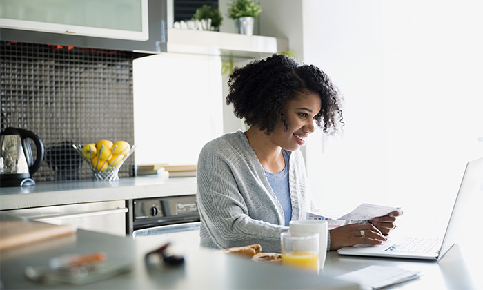 Woman with laptop in kitchen and bill in hand