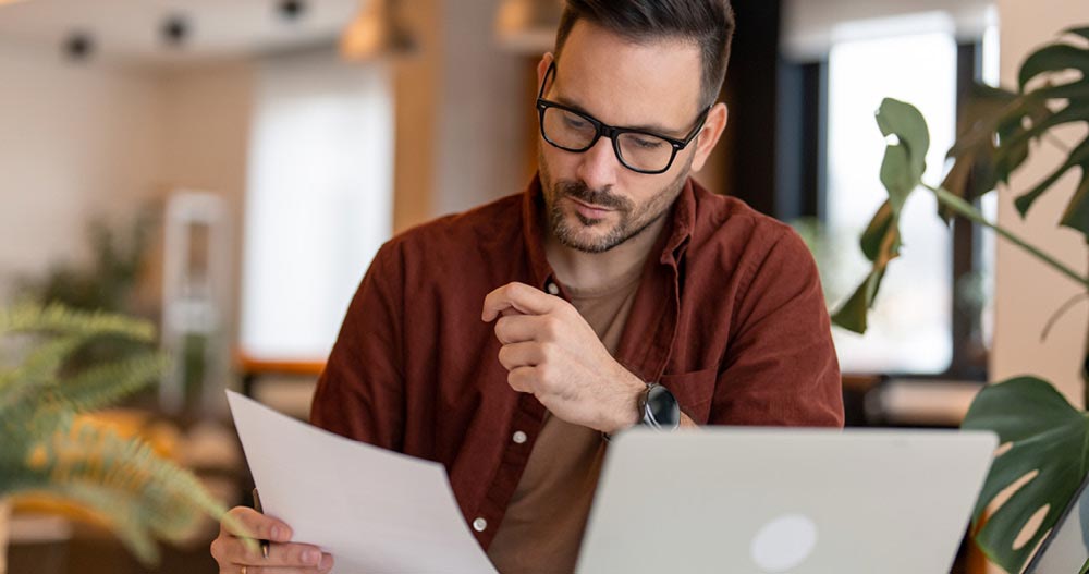 Man with a laptop reading a paper