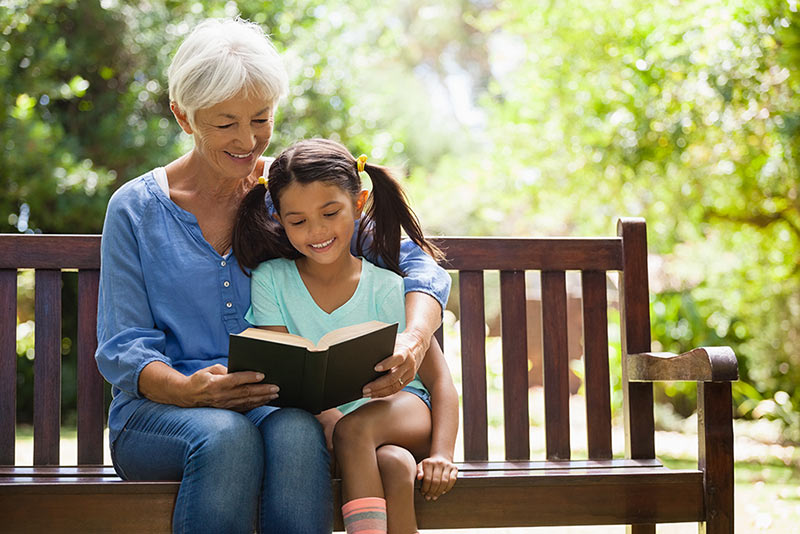 Grandmother and granddaughter on a bench reading a book outside