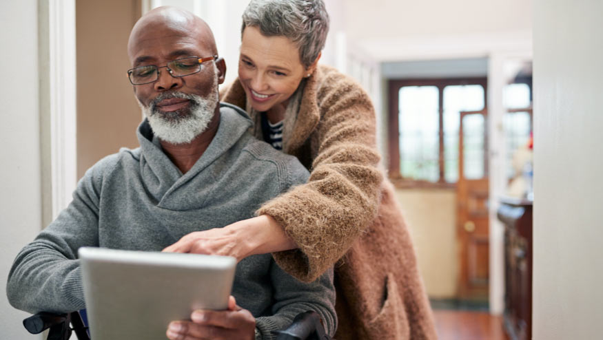 Medicare aged couple with man in wheelchair looking at tablet