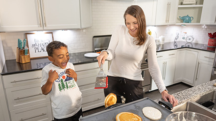 Mom and son cooking pancakes together in kitchen.