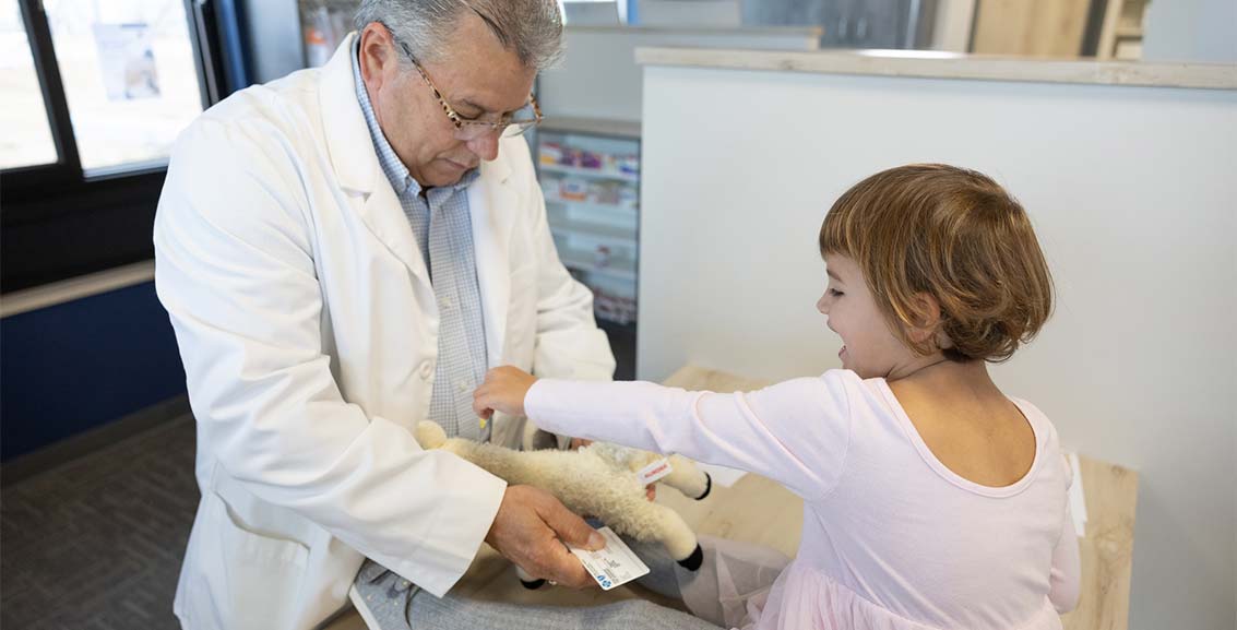 Pharmacist helps young child put bandage on stuffed animal. 