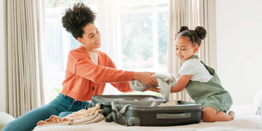 Mother and daughter packing suitcase for trip after checking their health insurance plan from Blue Cross Blue Shield of North Dakota.