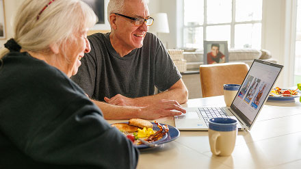Retired couple at kitchen table looking at a laptop