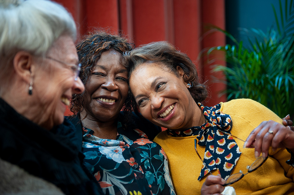 Three medicare-age women reconnecting, smiling and talking. 