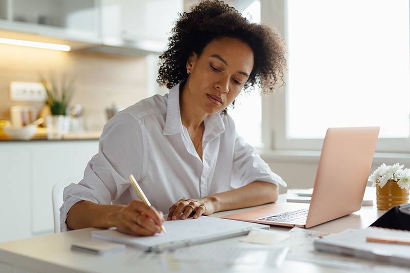 Woman looking at a laptop and writing notes
