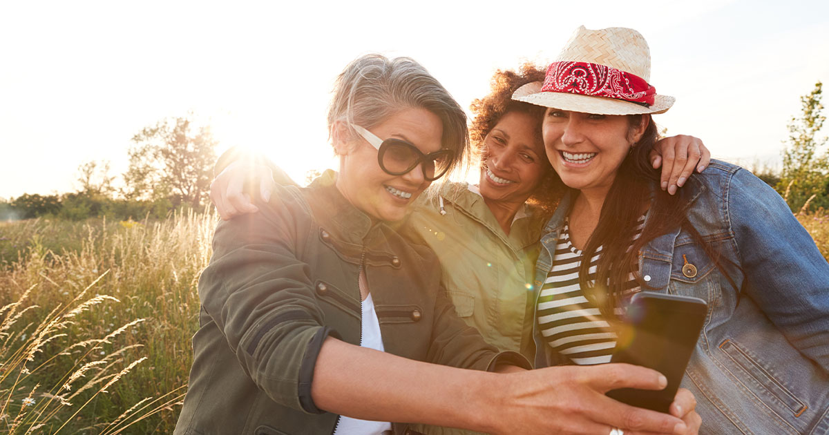 Group Of Mature Female Friends Walking Through Field On Camping Posing For Selfie