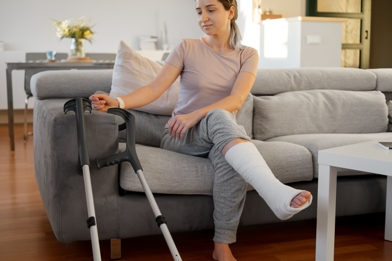 Woman in her late twenties on couch at home with elbow crutches and orthopedic plaster. Fracture of the leg or foot. Concept of rehabilitation and healing physiotherapy. Orthopedics and Traumatology.