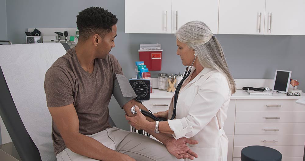 Senior caucasian doctor using stethoscope to measure patients blood pressure