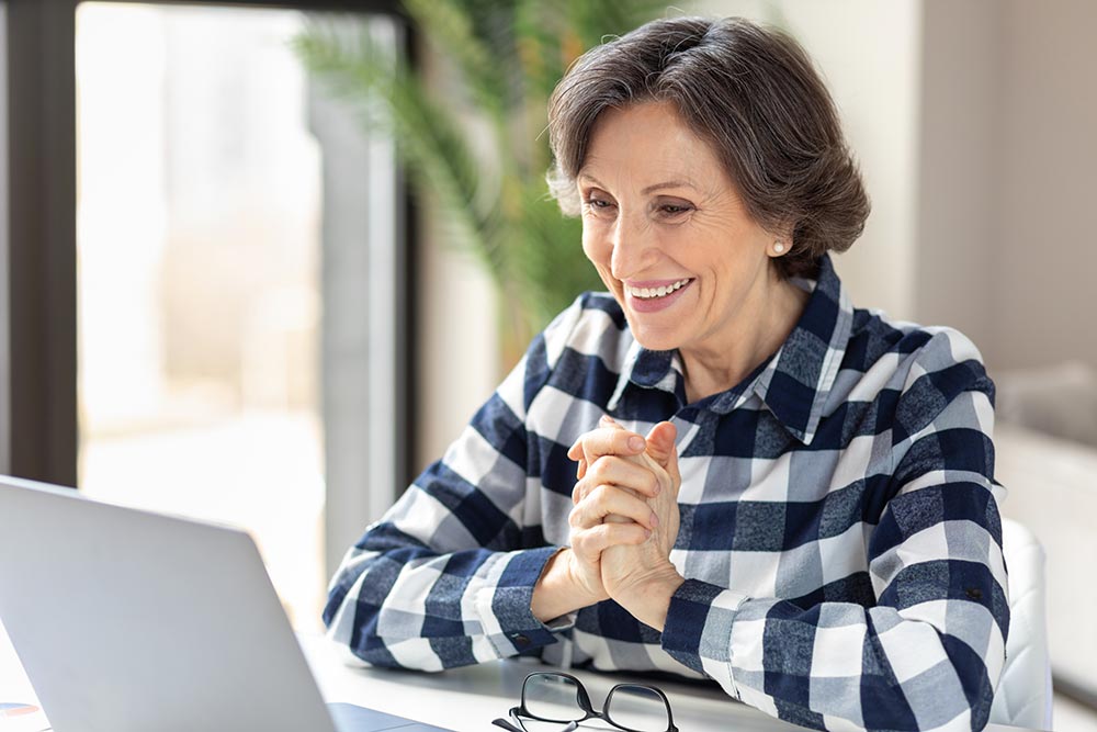 Medicare aged woman smiling and looking at a laptop