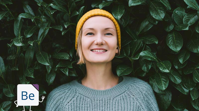 Smiling young woman standing in front of green leaves