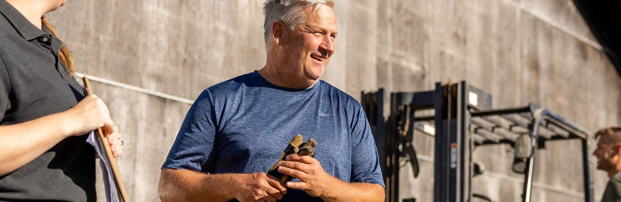 Middle aged man holding gloves near a farm building.