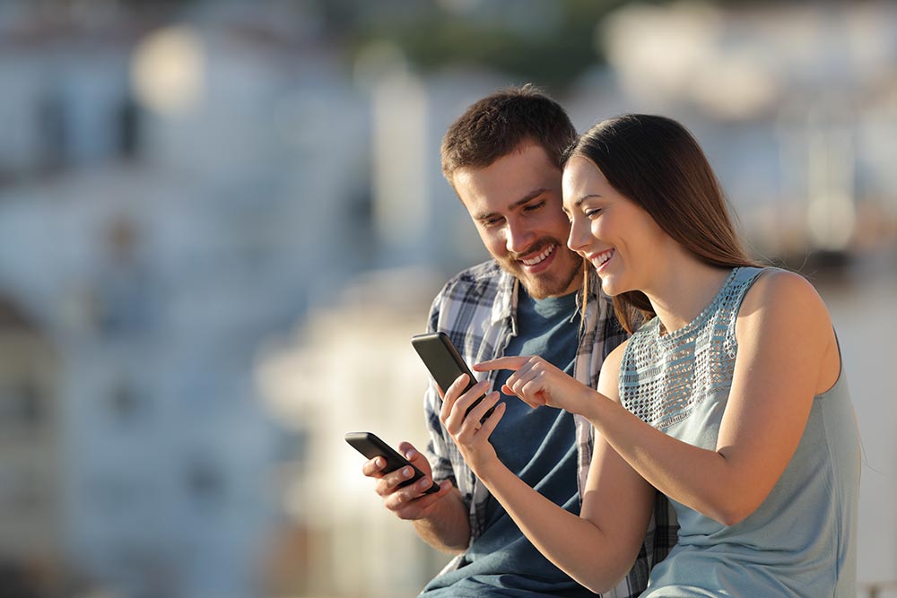 couple by the seashore looking at mobile phones