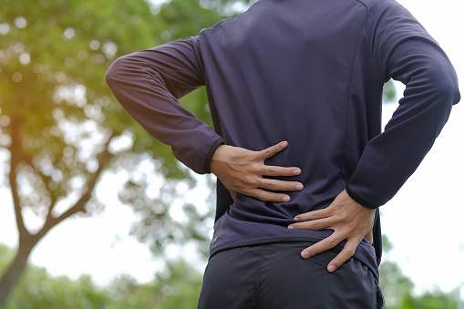 A person suffering from back pain with hands held on their back