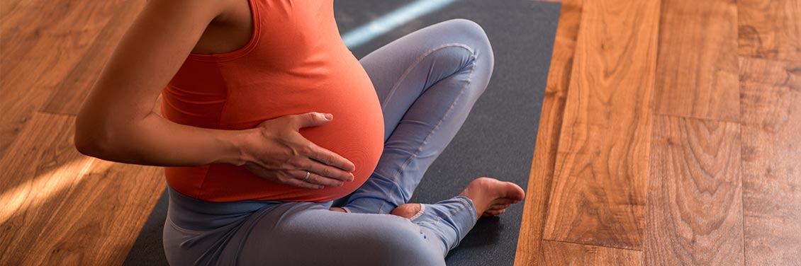 A pregnant woman sitting cross-legged on an exercise mat