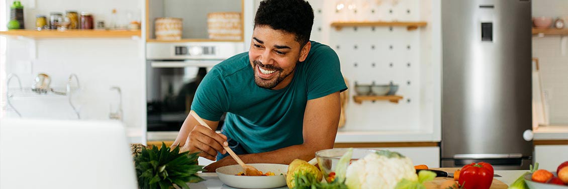 A smiling man cooking at home a watching a laptop screen