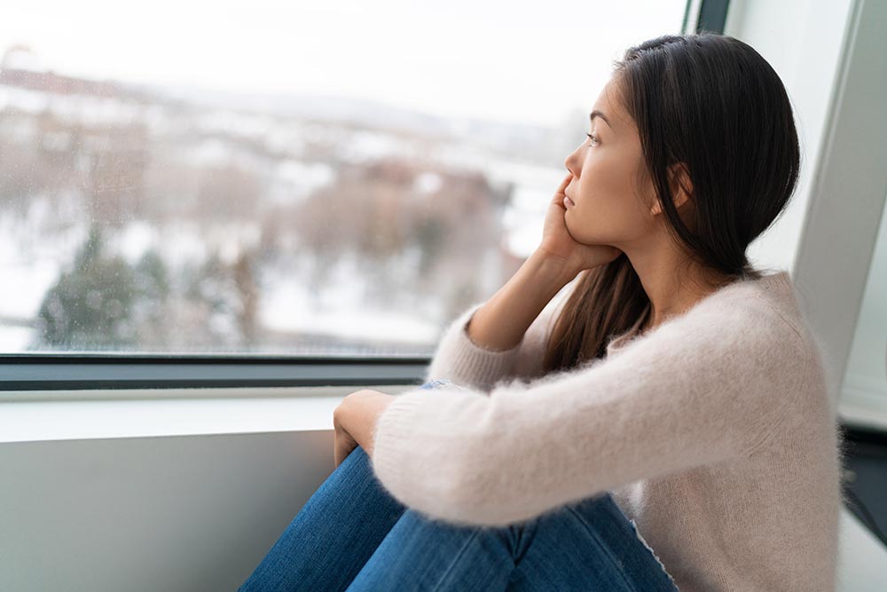 Asian girl feeling lonely looking out at winter landscape