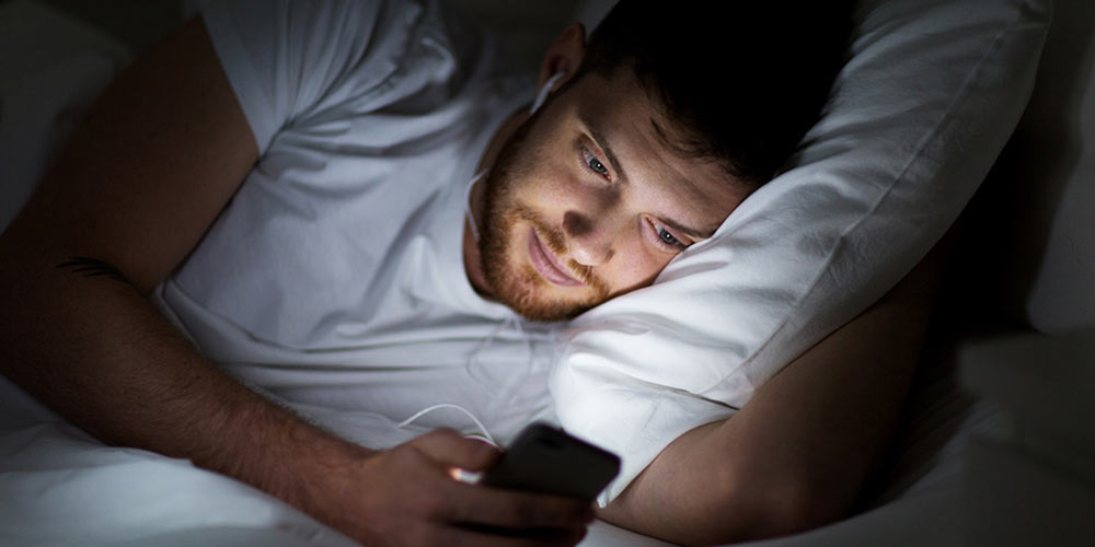 man with smartphone and earphones in bed at night