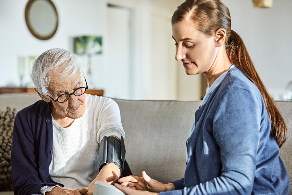 Woman checking elderly mans blood pressure at his home. 