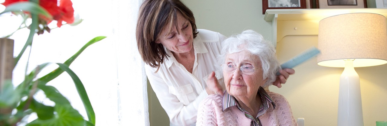 Middle-aged daughter combing and styling her elderly mother's hair. 