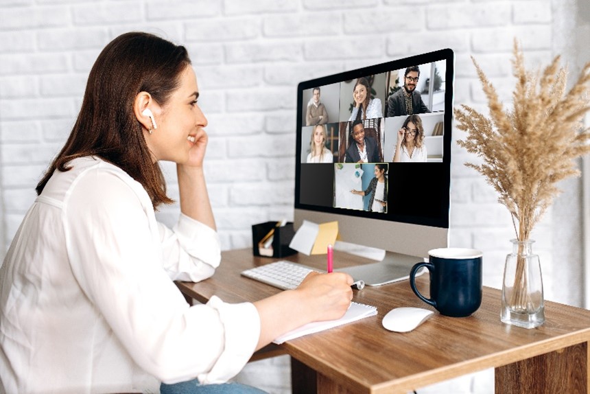 Woman sitting and working at desk with group video call on her computer.