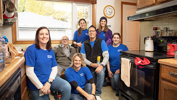Employee volunteers pose with an elderly man in his home