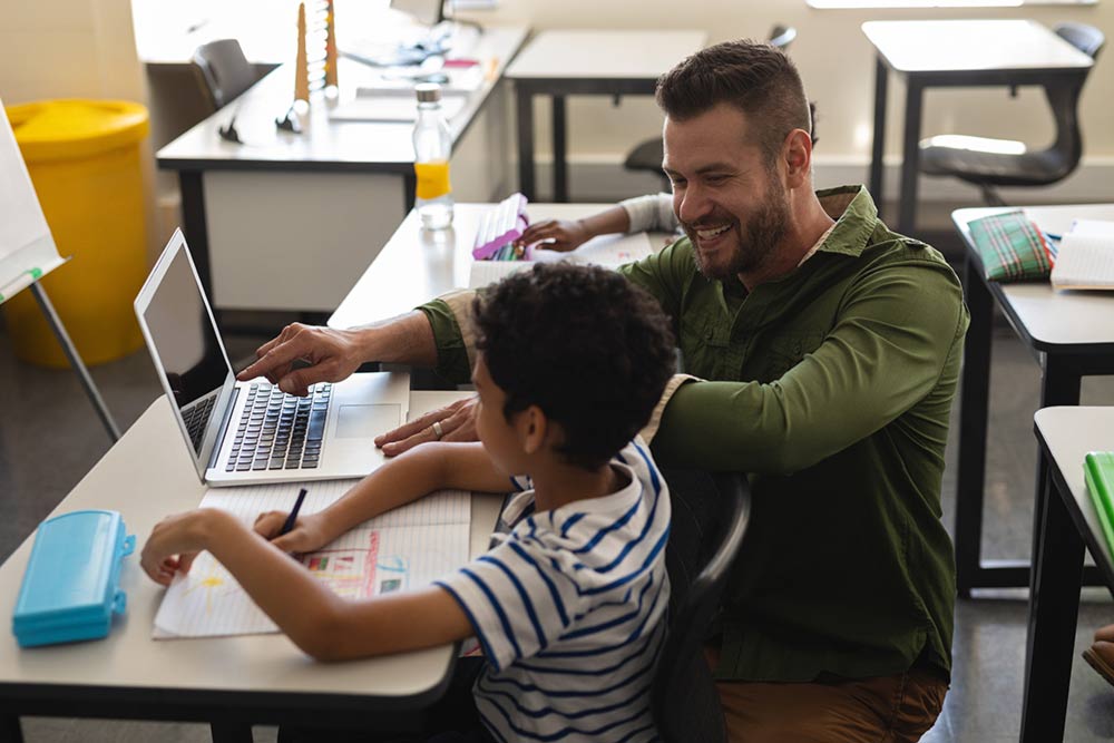 Young school teacher helping boy with study on laptop