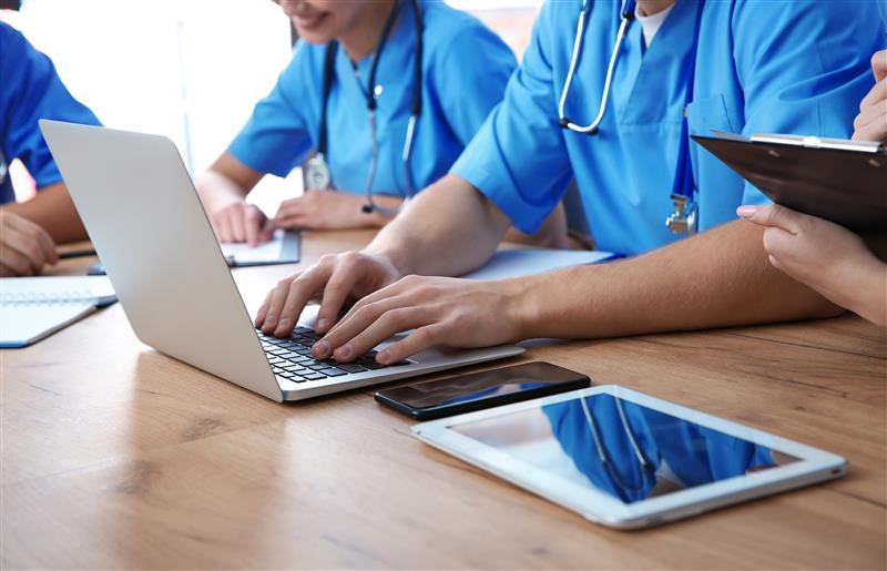 Healthcare professionals or students in blue scrubs working on laptops.