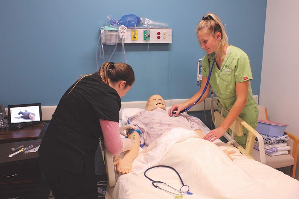 Photo of two nursing students from Dakota College at Bottineau, practicing taking vitals on a nursing manikin. 
