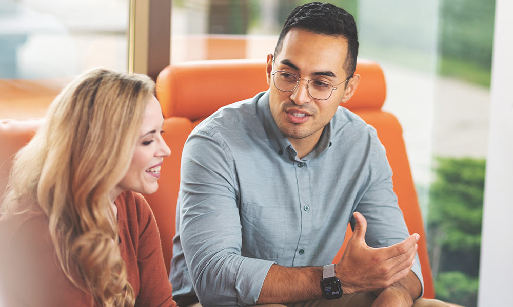 Two young professionals talking on a sofa.