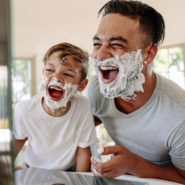 Father and young son with shaving cream on faces laughing