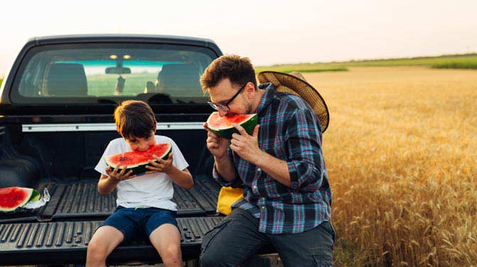 Father and son eating watermelon on a truck tailgate