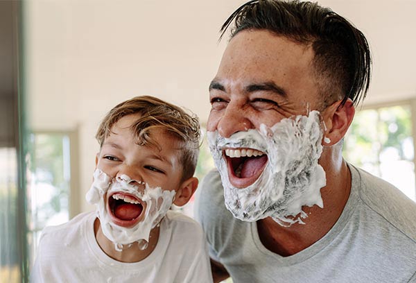 Father and young son with shaving cream on faces laughing