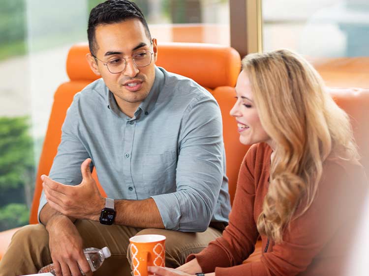 Two young professionals talking on a sofa.