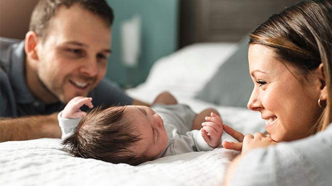 Mom and dad playing with newborn on a bed