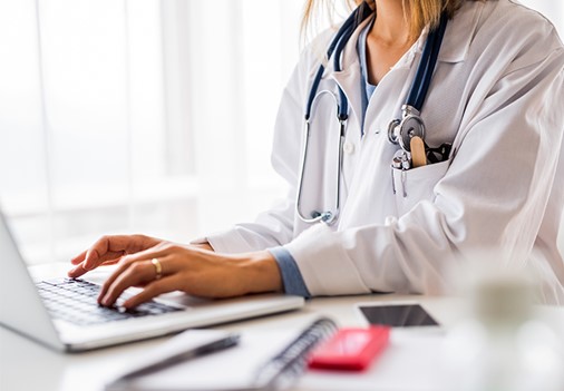 A physician typing on a laptop computer