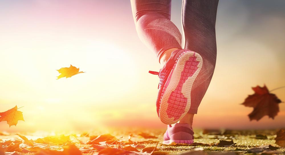 Woman in tennis shoes running through leaves